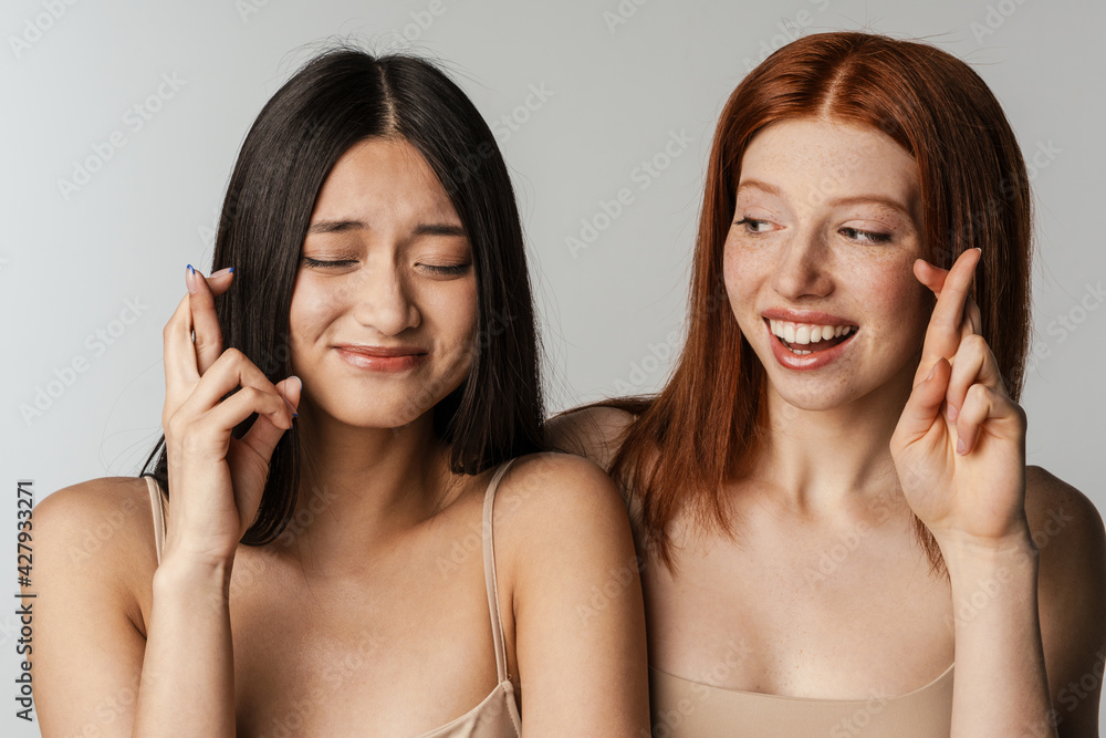 Multiracial two women smiling and holding fingers crossed for good luck