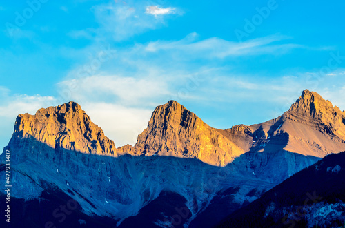 Scenery of high mountain peak at sunset (sunrise) and blue skay with white clouds. Contrast shadow.