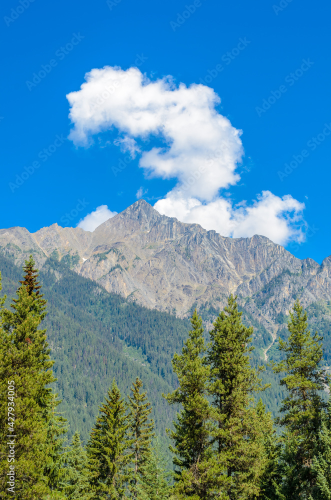 Scenery of high mountain peak over blue sky with white clouds and green foreground.