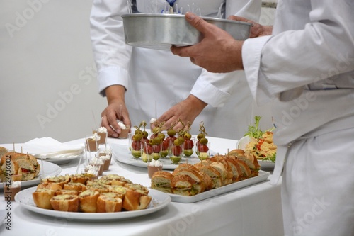 The chef and the waiter are setting the table with appetizers for the event.