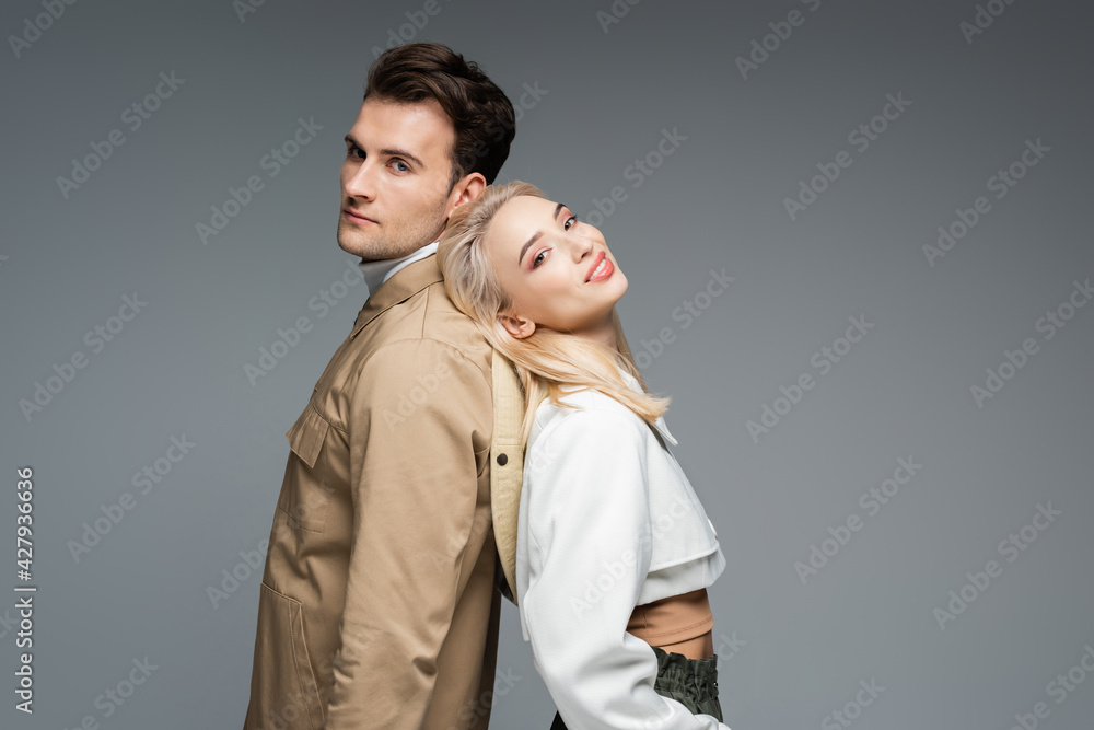 man in jacket standing back to back with cheerful blonde young woman isolated on grey man in jacket standing back to back with cheerful blonde young woman isolated on grey