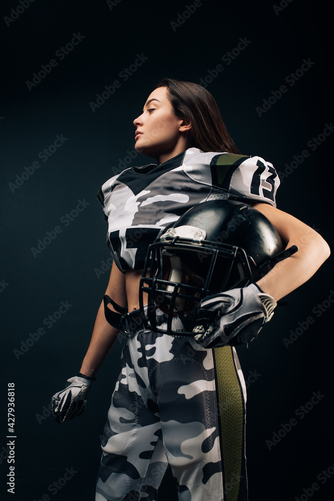 Naklejka premium Athletic woman poses in American football uniform with helmet in her hand.