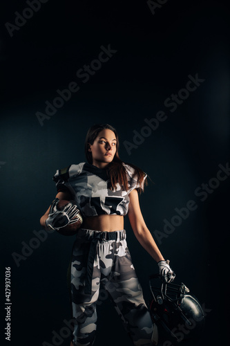 Athletic woman poses in American football uniform with helmet and ball in her hands.