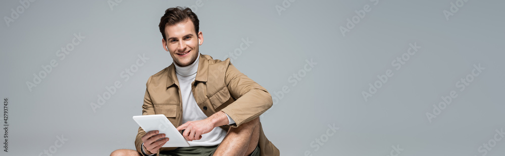 trendy man smiling while using digital tablet isolated on grey, banner trendy man smiling while using digital tablet isolated on grey, banner