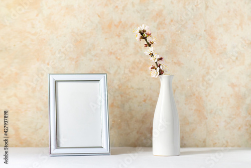 Blank vertical picture frame mock up on white  table. Blooming apricot branches in a white ceramic vase. Art concept. Scandinavian interior design  no people. Spring still life. 