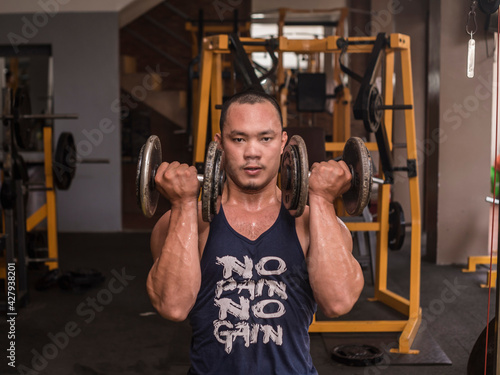Vászonkép A brawny and muscular asian man trains anterior deltoids at the gym