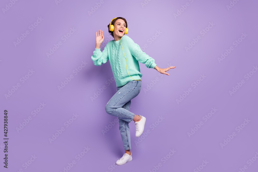 Full length body size photo of dancing cheerful girl listening music in yellow earphones laughing isolated pastel violet color background