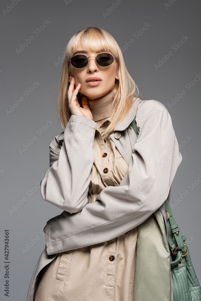 young fashionable woman in sunglasses and trench coat posing isolated on grey young fashionable woman in sunglasses and trench coat posing isolated on grey