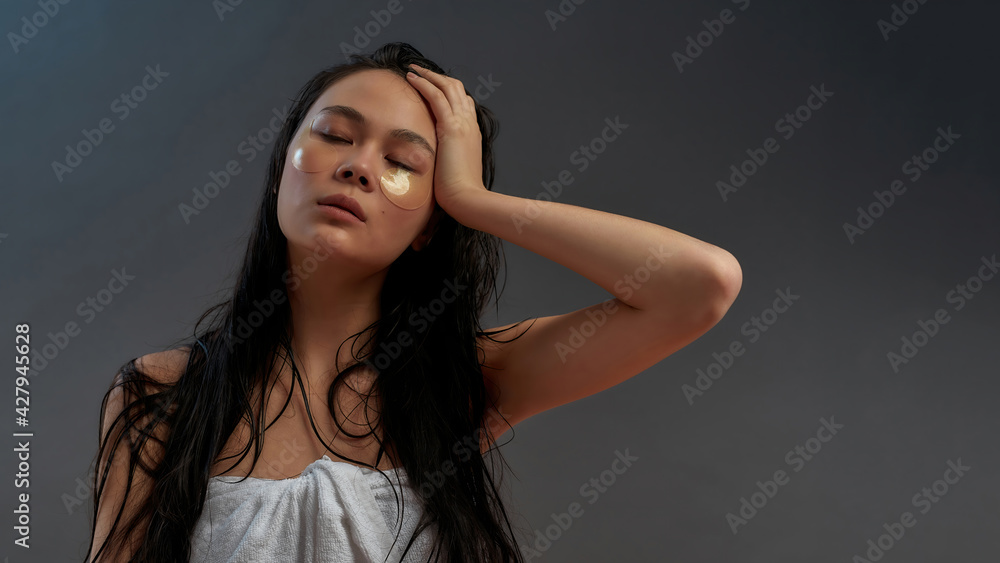 Young beautiful asian half naked woman in bath towel with cosmetic eye patches and hand on her head Young beautiful asian half naked woman in bath towel with cosmetic eye patches and hand on her head