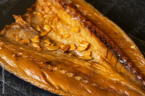 Cold smoked marinated mackerel or scomber opened fillet fish with spices, garlic on black stone plate over dark background. Mediterranean food, appetizer, seafood. Close up view with copy space.