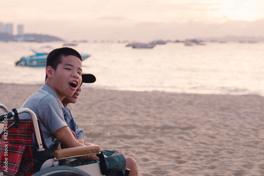 Fototapeta premium Asian special child on wheelchair is happily on the beach with parents in family holiday to travel and learning about nature around the sea beach,Life in the education age,Happy disabled kid concept.