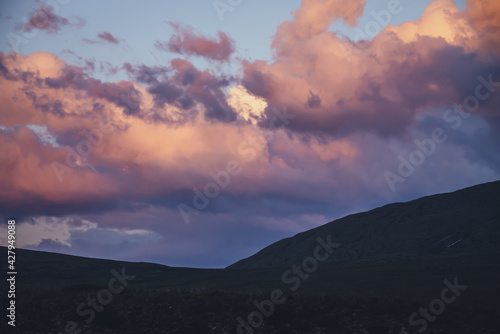 Atmospheric minimal mountain scenery with lilac dawn sky. Scenic minimalist landscape with purple sunset in mountains. Beautiful sunrise in mountains in pastel tones. Rocky mountain in dawn cloudy sky