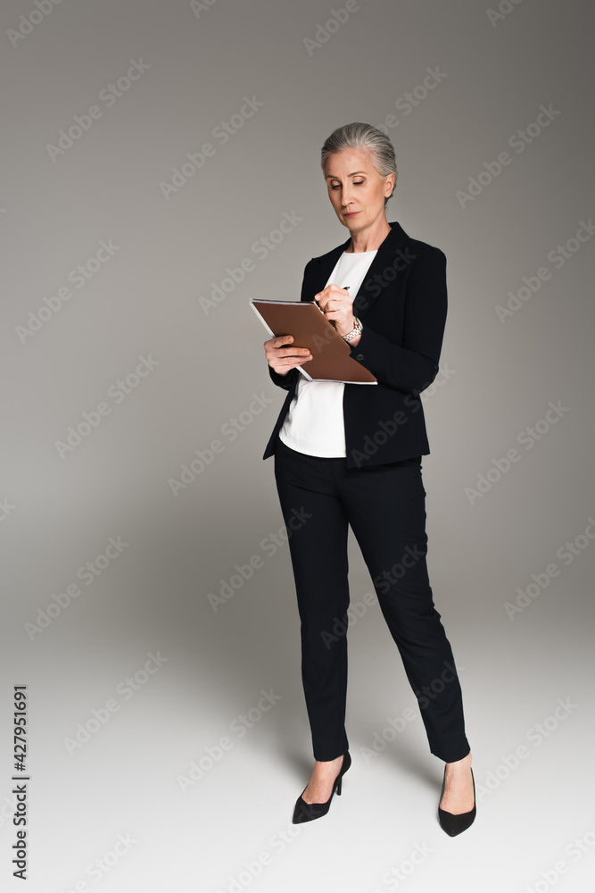 Businesswoman writing on paper folder on grey background Businesswoman writing on paper folder on grey background