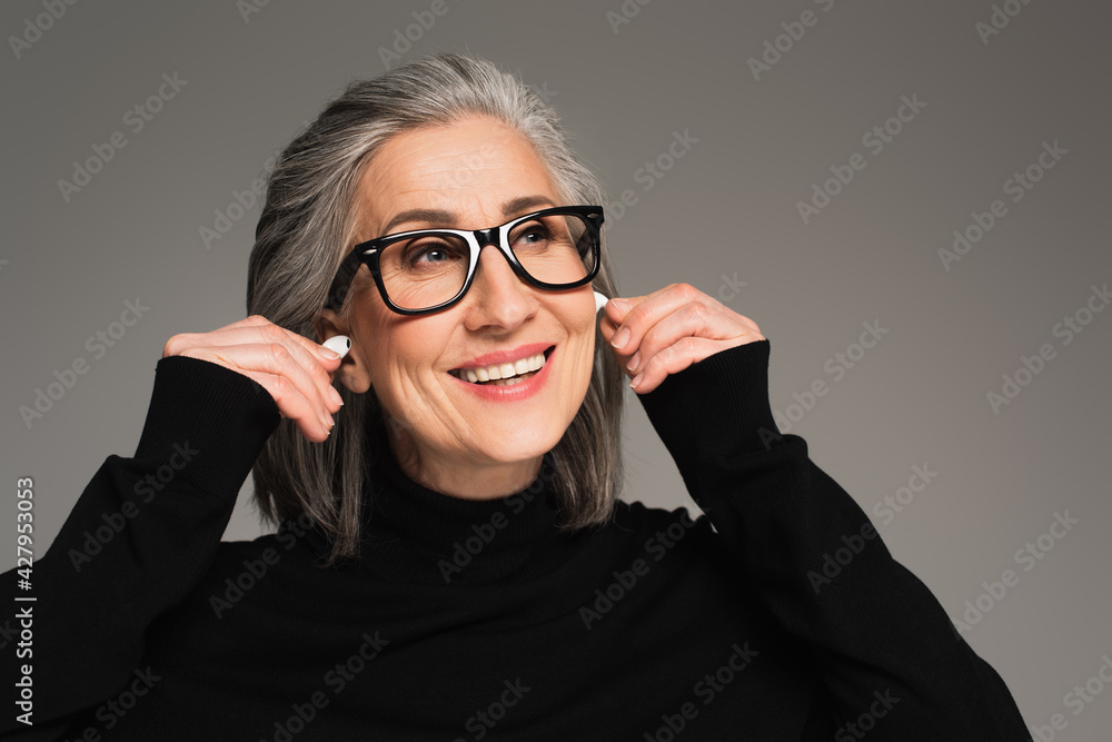 Smiling mature woman holding earphones isolated on grey Smiling mature woman holding earphones isolated on grey