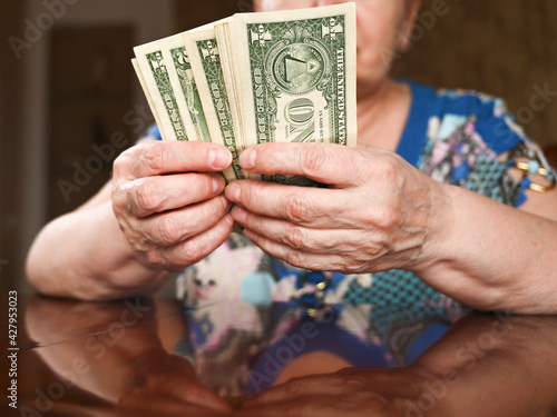 An elderly woman counts dollars. Last money for life, low incomes, poverty, 1 dollar bills.
