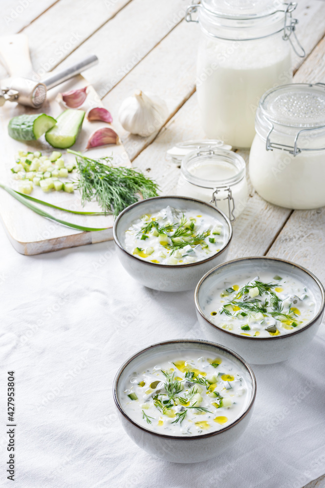 Traditional summer cold soup of homemade yogurt, cucumbers and fresh herbs on a table Traditional summer cold soup of homemade yogurt, cucumbers and fresh herbs on a table