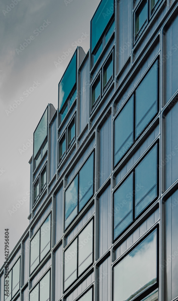 Vistas de un edificio con ventanas de marco redondeado desde abajo. Arquitectura contemporánea, con grandes ventanales de cristal que muestran el reflejo del cielo en tonos azulados y turquesa Vistas de un edificio con ventanas de marco redondeado desde abajo. Arquitectura contemporánea, con grandes ventanales de cristal que muestran el reflejo del cielo en tonos azulados y turquesa