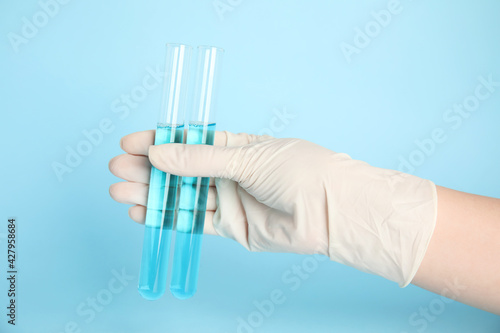 Scientist holding test tubes with liquid on turquoise background, closeup