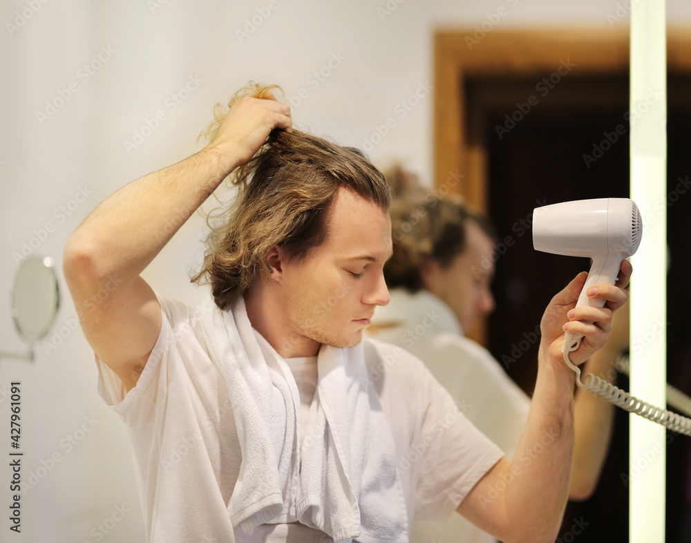 man in the bathroom drying his hair with a hairdryer man in the bathroom drying his hair with a hairdryer
