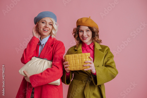 Spring fashion, shoppung, sale, discount,  conception: happy smiling elegant women wearing stylish colorful clothes, holding trendy leather bags posing on pink background. Copy, empty space for text photo