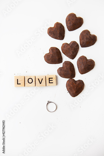 Truffle chocolate candies in the form of a heart on a white background. Inscription love made of wooden letters and a ring with a diamond. Hand and serge proposals, valentine. photo