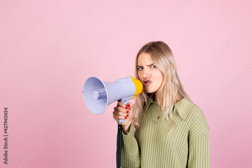 Pretty european woman in casual sweater on pink background angry shouting in megaphone loudspeaker, attention Pretty european woman in casual sweater on pink background angry shouting in megaphone loudspeaker, attention