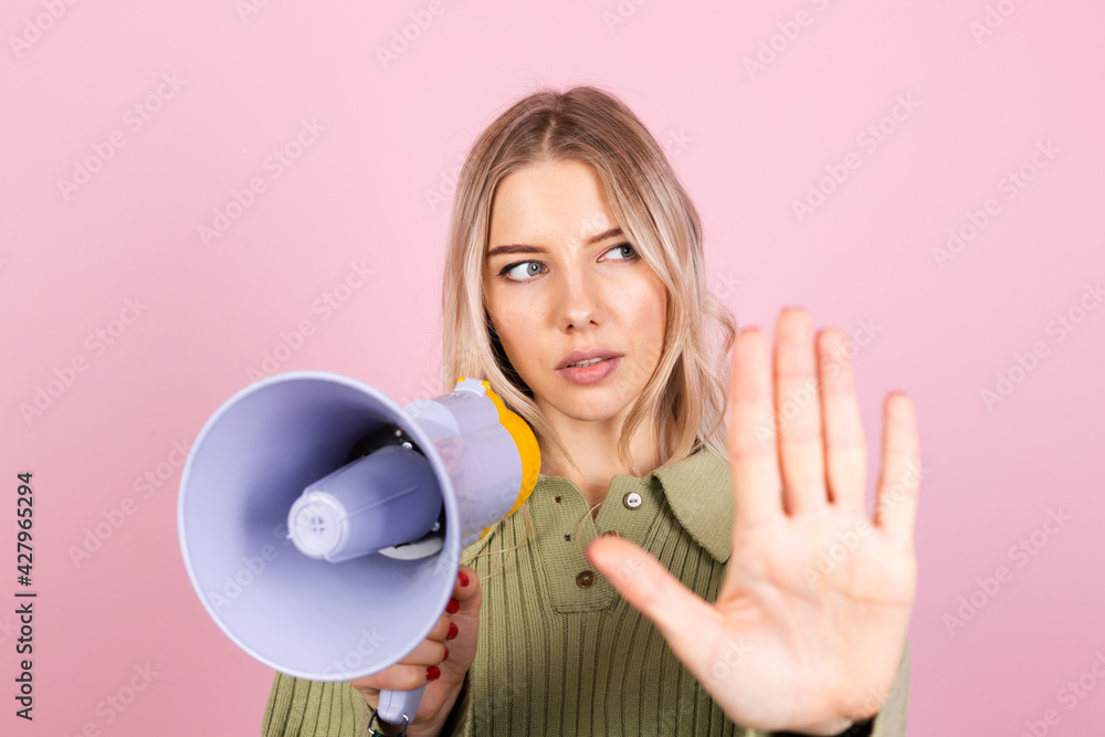 Pretty european woman in casual sweater on pink background unhappy serious with megaphone doing stop sign with palm of the hand. Warning expression Pretty european woman in casual sweater on pink background unhappy serious with megaphone doing stop sign with palm of the hand. Warning expression