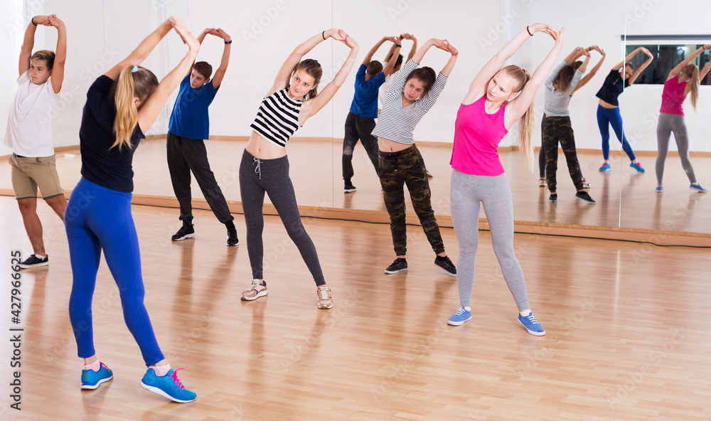 Group of teenage students with female trainer stretching at dance class