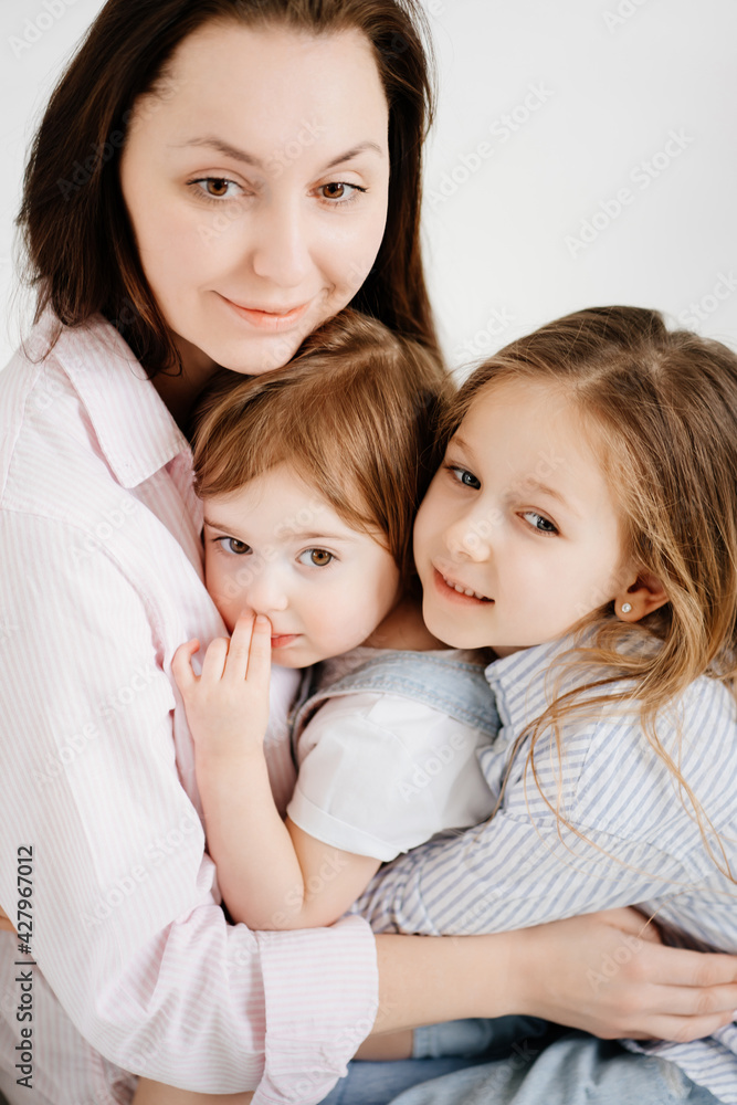 happy family sit on floor and cuddle in white photo studio.Mom and two daughters happy family sit on floor and cuddle in white photo studio.Mom and two daughters