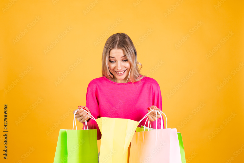 Pretty european woman in pink  blouse on yellow background holding shopping bags surprised shocked emotions, discount sale promotion concept