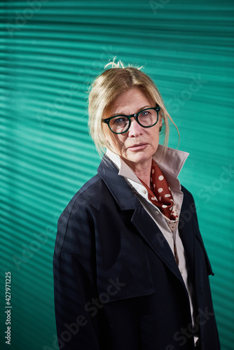 Portrait of stylish mature woman in eyeglasses looking at camera against the green background