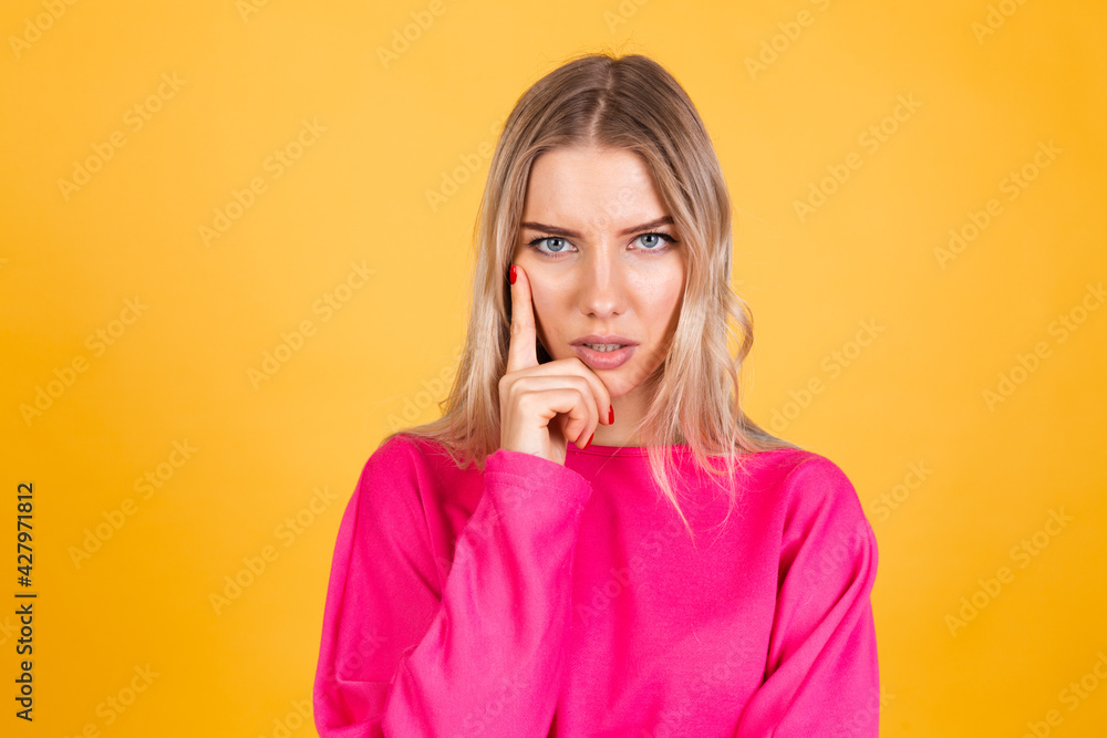 Pretty european woman in pink blouse on yellow background looks to camera thoughtfully with serious face focused Pretty european woman in pink blouse on yellow background looks to camera thoughtfully with serious face focused