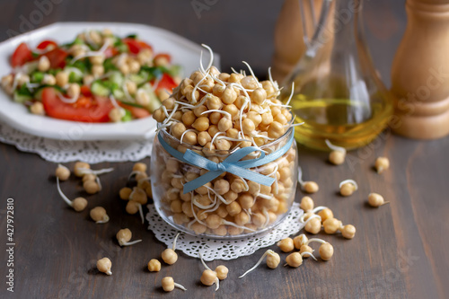 Sprouted chickpeas in glass jar. Fresh salad with tomato cucumber chickpeas and olive oil on background . Raw vegan healthy food concept. Wooden background.
