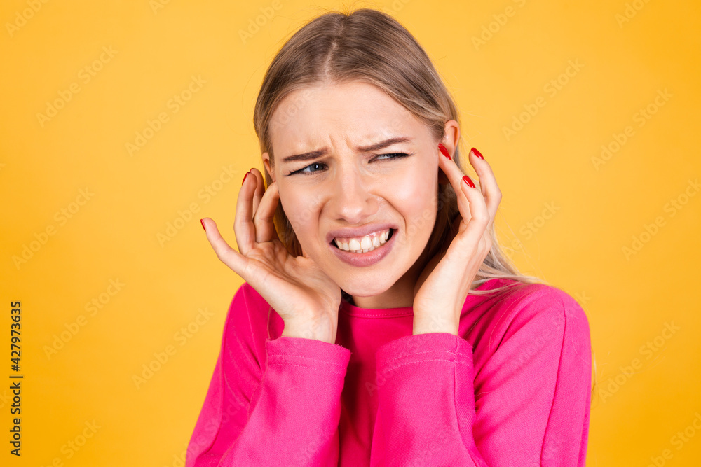 Pretty european woman in pink blouse on yellow background covering ears with fingers with annoyed expression for the noise of loud music Pretty european woman in pink blouse on yellow background covering ears with fingers with annoyed expression for the noise of loud music