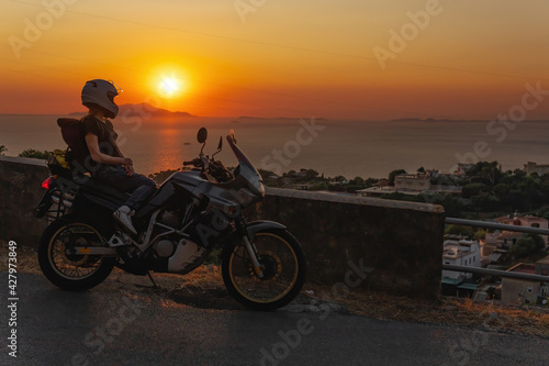 Biker girl sits on a adventure motorcycle. Freedom lifestyle concept. Romantic sunset. Sea and mountains  Copy space. Capri island. Sorrento Italy