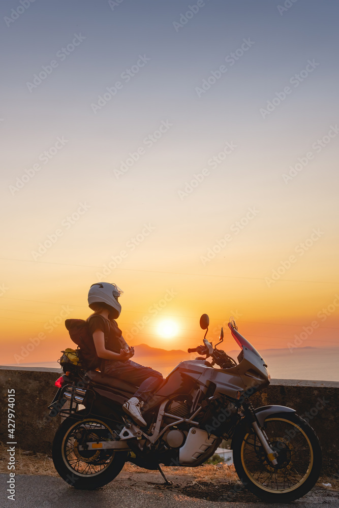 Biker girl sits on a adventure motorcycle. Freedom lifestyle concept. Romantic sunset. Sea and mountains, Vertical photo. Capri island. Sorrento Italy