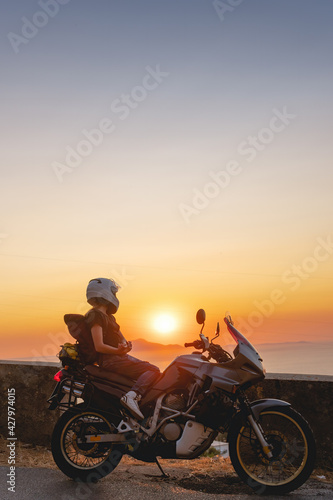 Biker girl sits on a adventure motorcycle. Freedom lifestyle concept. Romantic sunset. Sea and mountains, Vertical photo. Capri island. Sorrento Italy