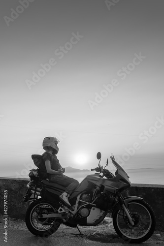 Biker girl sits on a adventure motorcycle. Freedom lifestyle concept. Romantic sunset. Sea and mountains, Black and white. Vertical photo. Capri island. Sorrento Italy