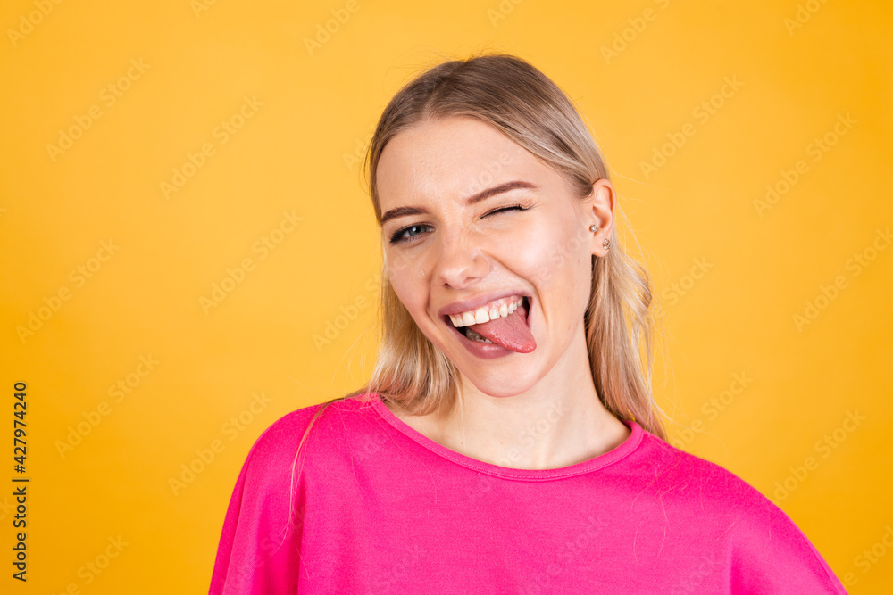 Pretty european woman in pink blouse on yellow background sticking tongue out happy with funny expression does funny grimaces Pretty european woman in pink blouse on yellow background sticking tongue out happy with funny expression does funny grimaces