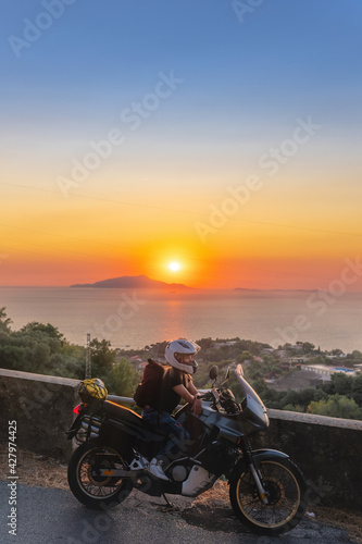 Biker girl sits on a adventure motorcycle. Freedom lifestyle concept. Romantic sunset. Sea and mountains  Vertical photo. Capri island. Sorrento Italy