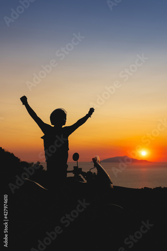 Silhouette of Biker man and his adventure motorcycle. Enjoying perfect sunset view. Freedom concept. Travel and tourism. arms spread out to the sides