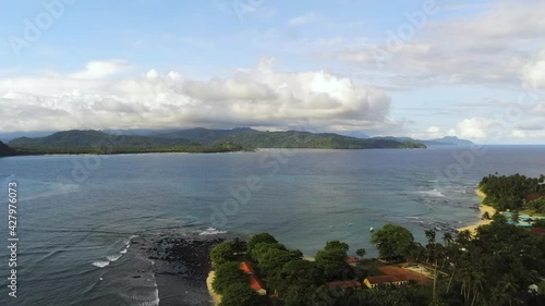 Aerial view over palm trees, revealing the ocean, sunny evening, in Ilheu das Rolas - rising, drone shot photo