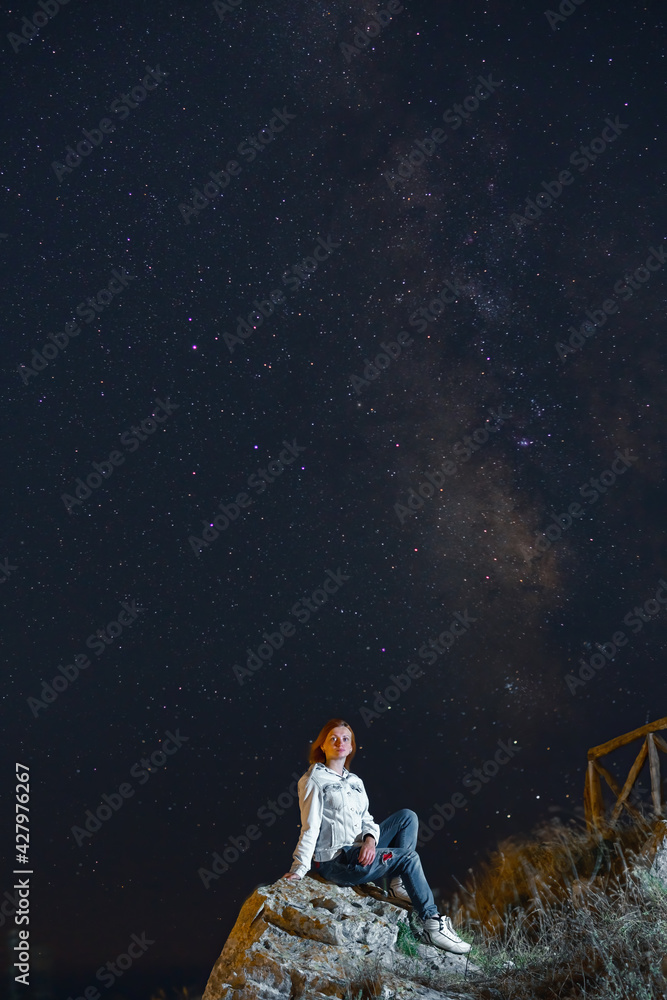 Girl alone enjoying watched the star and milky way galaxy over the sky on top of the mountain. Night landscape with beautiful sky. Vertical photo