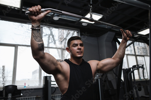 Attractive muscular bodybuilder working out on lat pulldown gym machine