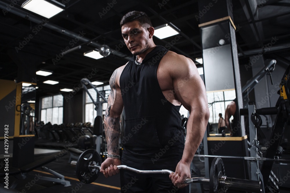 Strong muscular bodybuilder lifting barbell at the gym Strong muscular bodybuilder lifting barbell at the gym