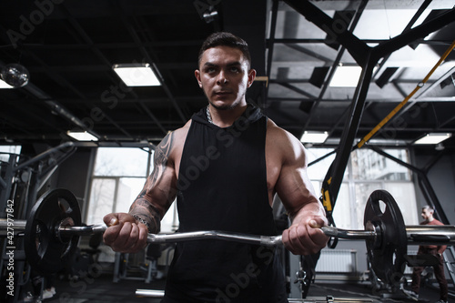 Focused ripped male athlete exercising with barbell at the gym