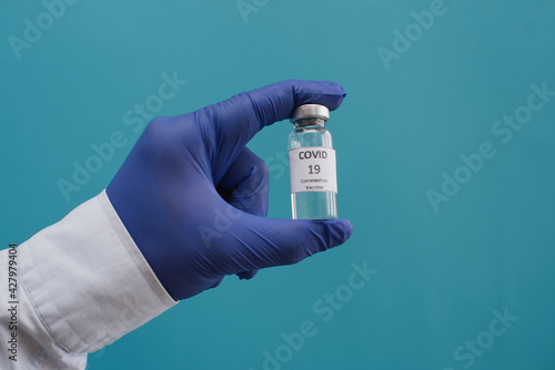 Male hands hold vial of Covid - 19 vaccine in bottle for injection on blue background. Place for text