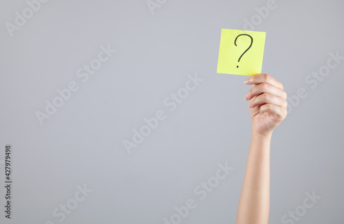 Young woman holding a question mark in her hand.