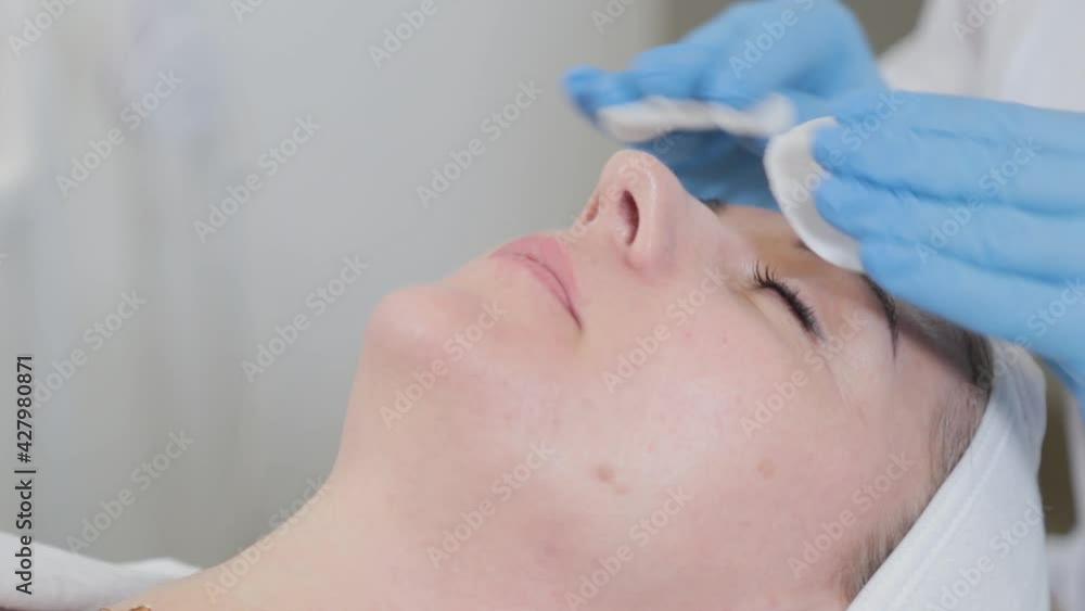 Professional beautician woman wipes face with cotton pads to client. Professional beautician woman wipes face with cotton pads to client.