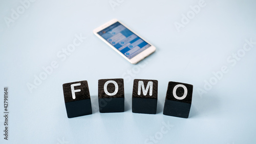 FOMO, Fear of missing out, social anxiety, stay continually connected, fear of regret, Social networking. FOMO text with blurred cell phone with social Media icons on blue background photo